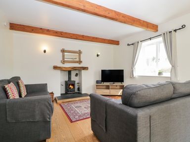 A living room with two gray sofas a wood burning stove a tv on a stand and wooden ceiling beams at Glen Cottage Troutbeck near Keswick
