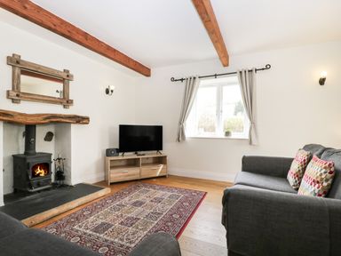 A living room with a wood burning stove tv on a wooden stand patterned rug and gray sofas at Glen Cottage in Troutbeck near Keswick