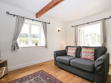 A living room with a two-seater sofa and patterned cushions near windows with curtains at Glen Cottage in Troutbeck near Keswick