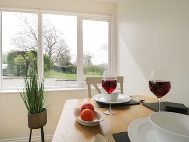 A dining table with plates glasses of red wine a bowl of fruit and a plant near a window at Glen Cottage in Troutbeck near Keswick