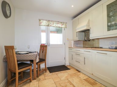 A kitchen with a wooden table and two chairs beside a door and white cabinets at Glen Cottage in Troutbeck near Keswick