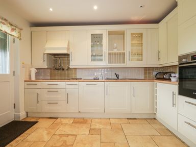 A kitchen with white cabinets a tiled floor a built in oven and a window at Glen Cottage in Troutbeck near Keswick