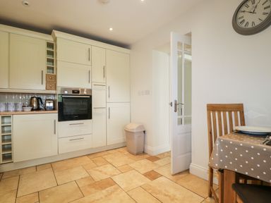 A kitchen with cream cabinets a built-in oven a trash bin and a dining table with a polka dot tablecloth at Glen Cottage Troutbeck near Keswick