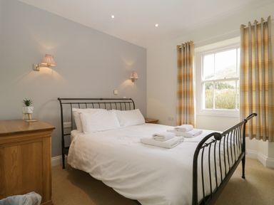A bedroom with a metal bed frame white bedding folded towels bedside tables curtains and a wooden chest of drawers at Glen Cottage in Troutbeck near Keswick