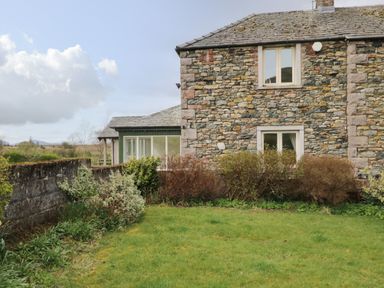 A stone house with a grassy garden and shrubbery near a stone wall at Glen Cottage in Troutbeck near Keswick