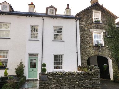 A row of connected houses with white and stone exteriors and green door at Oak Cottage in Windermere
