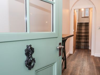A hallway with a mint green door opening to a wooden floor and stairs with plaid carpet at Oak Cottage in Windermere