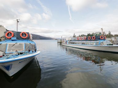 Two passenger boats docked on a lake with hills and trees in the background at Oak Cottage in Windermere