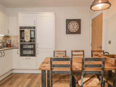 A kitchen with white cabinets wooden dining table with metal chairs and a wall clock at Oak Cottage in Windermere
