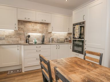 A kitchen with white cabinets wooden dining table and chairs and built in oven at Oak Cottage Windermere