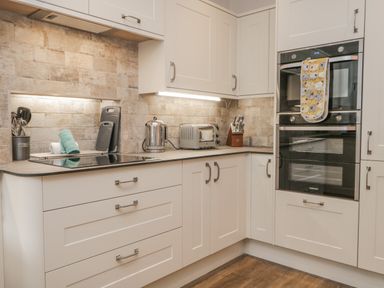 A kitchen with white cabinets a built-in oven kettle toaster and utensils at Oak Cottage in Windermere