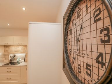 A kitchen with white cabinets a stove and a large wall clock with a metal grid at Oak Cottage in Windermere