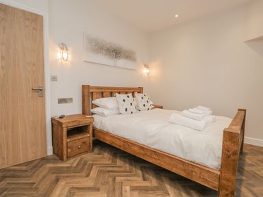 A bedroom with a wooden bed and bedside tables with lamps on the walls at Oak Cottage in Windermere
