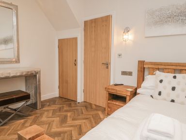 A bedroom with wooden doors wooden bed side table and a metal desk with a bench at Oak Cottage in Windermere