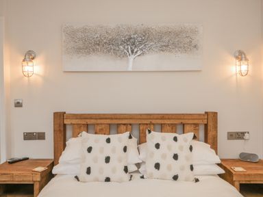 A bedroom with a wooden bed frame and two patterned pillows two wooden bedside tables and wall-mounted lights at Oak Cottage in Windermere