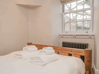 A bedroom with a wooden bed frame white towels on the bed and a window with a view of stone buildings at Oak Cottage in Windermere