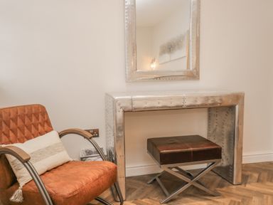 An armchair with a cushion next to a metallic desk with a stool and a mirror on the wall at Oak Cottage in Windermere
