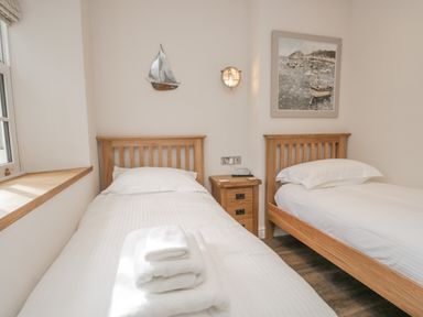 A bedroom with two wooden single beds a wooden bedside table between the beds a window on the left wall and nautical-themed wall art at Oak Cottage in Windermere