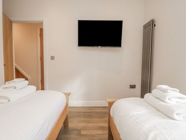 A bedroom with two single beds facing a wall mounted TV and a tall radiator at Oak Cottage in Windermere