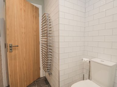 A bathroom corner with a toilet a wooden door and a chrome towel radiator on tiled walls at Oak Cottage in Windermere