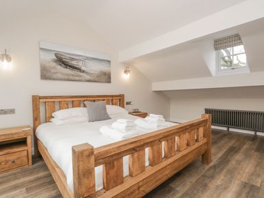 A bedroom with a wooden bed frame white bedding and folded towels on the bed at Oak Cottage in Windermere