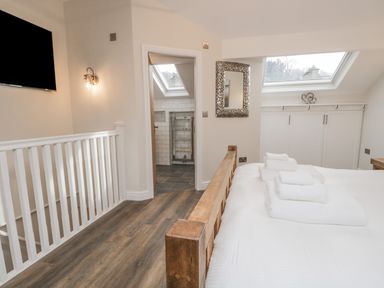 A bedroom with a wooden bed and folded towels by a staircase and a bathroom entrance at Oak Cottage in Windermere