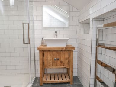 A bathroom with a wooden vanity unit and white sink next to a glass shower at Oak Cottage in Windermere