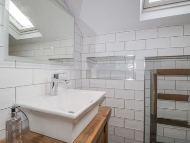 A bathroom sink with a faucet soap dispenser and tiled walls with a mirror and a skylight at Oak Cottage in Windermere