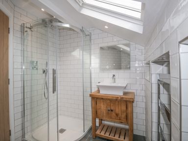 A bathroom with a corner shower enclosure wooden vanity unit with sink and skylight window at Oak Cottage in Windermere