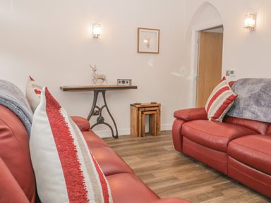 A living room with red leather sofas striped cushions wooden floor table with a metal base and a deer statue at Oak Cottage in Windermere