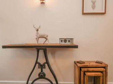 A wooden table with a metal base holding a decorative deer figure and a metal box beside a set of nested wooden stools