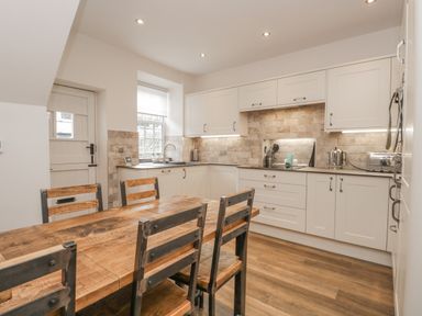 A kitchen with wooden table and chairs white cabinets and tiled backsplash at Oak Cottage in Windermere