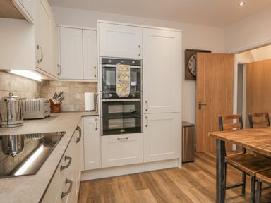 A kitchen with white cabinets double oven toaster kettle and wooden dining table with chairs at Oak Cottage in Windermere