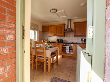 A kitchen with wooden cabinets and a dining table set with plates and wine bottles at Barcud Cottage Golden Grove near Llandeilo