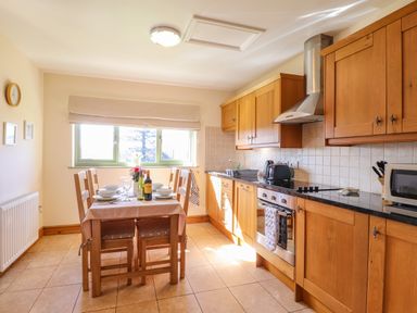 A kitchen with wooden cabinets a dining table set for four and kitchen appliances at Barcud Cottage in Golden Grove near Llandeilo