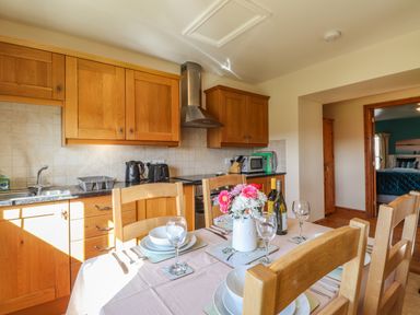 A kitchen with wooden cabinets a dining table set with dishes glasses and flowers at Barcud Cottage in Golden Grove near Llandeilo