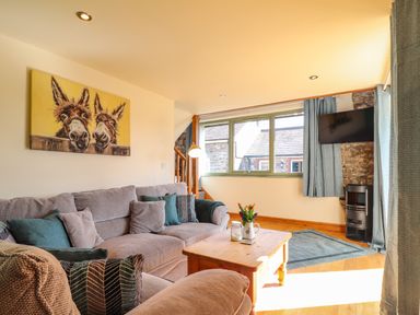 A living room with a grey sofa cushions a wooden coffee table and a mounted TV at Barcud Cottage in Golden Grove near Llandeilo