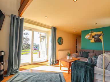 A living room with a wooden coffee table and sofas near glass patio doors at Barcud Cottage in Golden Grove near Llandeilo