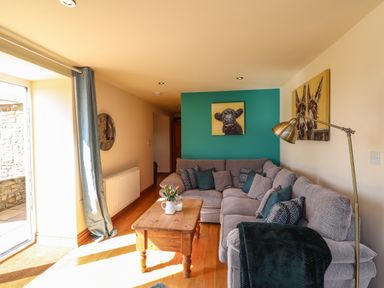 A living room with a grey corner sofa green cushions wooden coffee table and animal paintings at Barcud Cottage in Golden Grove near Llandeilo