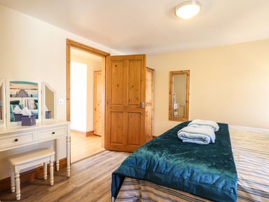 A bedroom with a bed covered with striped sheets and teal blanket towels on top and a white dressing table with a mirror and a stool at Barcud Cottage Golden Grove near Llandeilo