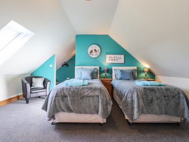 A bedroom with two single beds a armchair and slanted ceilings at Barcud Cottage in Golden Grove near Llandeilo