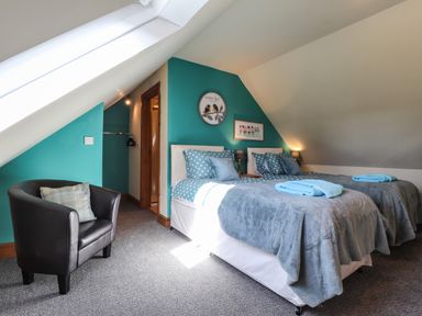 A bedroom with two single beds blue bedding and a black armchair at Barcud Cottage Golden Grove near Llandeilo