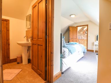 A bedroom with a polka dot bedspread and an adjacent bathroom with a sink at Barcud Cottage Golden Grove near Llandeilo