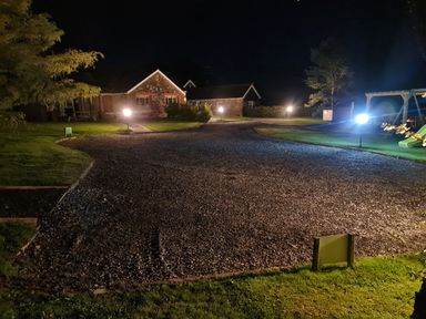 A gravel driveway with lights leading to stone houses and a children's play area at Barcud Cottage in Golden Grove near Llandeilo