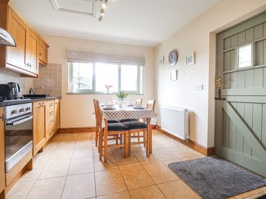 A kitchen with wooden cabinets a dining table with chairs and set table near a window and a green door at Gwennol Cottage in Golden Grove near Llandeilo