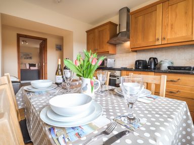 A kitchen with wooden cabinets a dining table set with white dishes glasses cutlery and a vase of tulips at Gwennol Cottage Golden Grove near Llandeilo