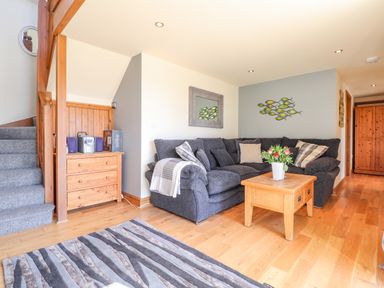 A living room with a gray sectional sofa a wooden coffee table with flowers a striped rug wooden stairs and a wooden cabinet at Gwennol Cottage Golden Grove near Llandeilo