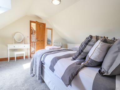 A bedroom with a bed and pillows a mirror on the wall and a dressing table with a stool at Gwennol Cottage in Golden Grove near Llandeilo
