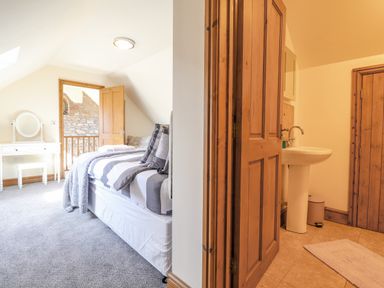 A bedroom with a bed and a dressing table next to a bathroom with a sink and wooden doors at Gwennol Cottage in Golden Grove near Llandeilo