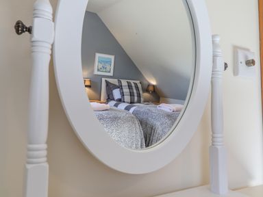 A bedroom with two single beds viewed through a round white mirror at Gwennol Cottage in Golden Grove near Llandeilo